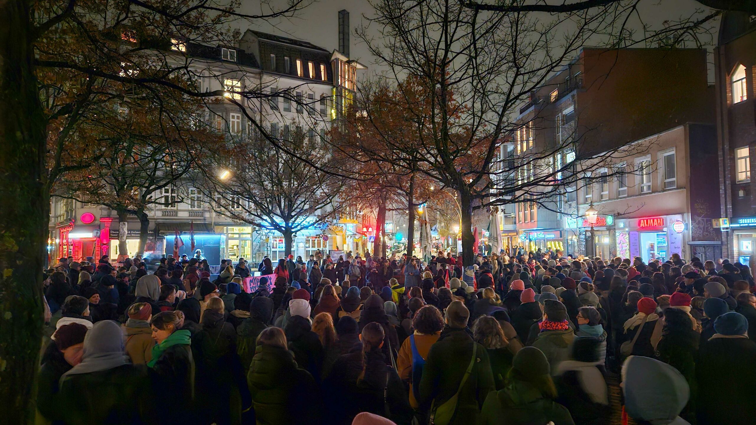 Vielen Menschen stehen auf einem Platz in Ottensen. im Hintergrund sind die Lichter der Läden.