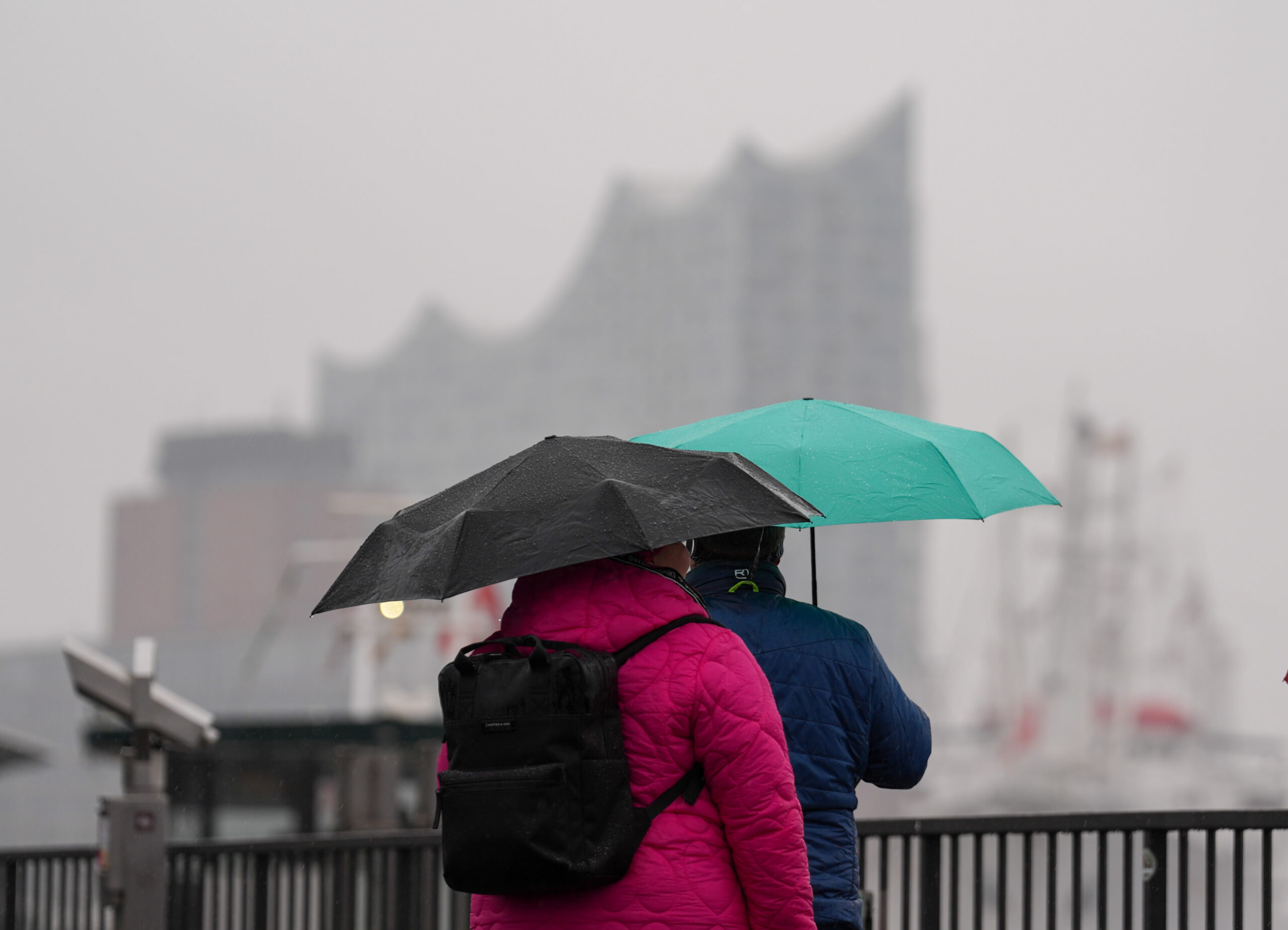 Passanten schützen sich mit ihren Regenschirmen vor dem Dauerregen an den Landungsbrücken.