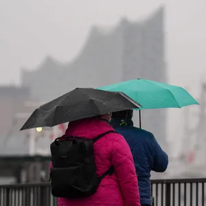 Passanten schützen sich mit ihren Regenschirmen vor dem Dauerregen an den Landungsbrücken.