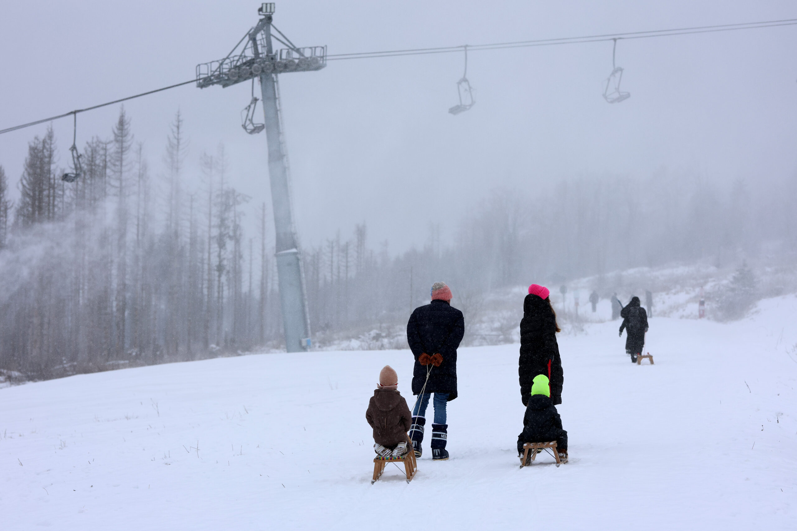 Eine Familie mit Schlitten läuft über den verschneiten Wurmberg im Harz.