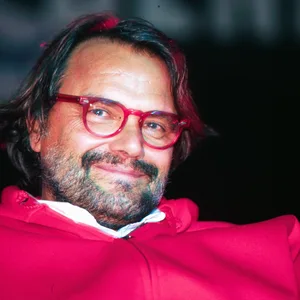 Der italienische Fotograf trägt einen roten Pulli und eine Brille. Er lächelt in die Kamera
