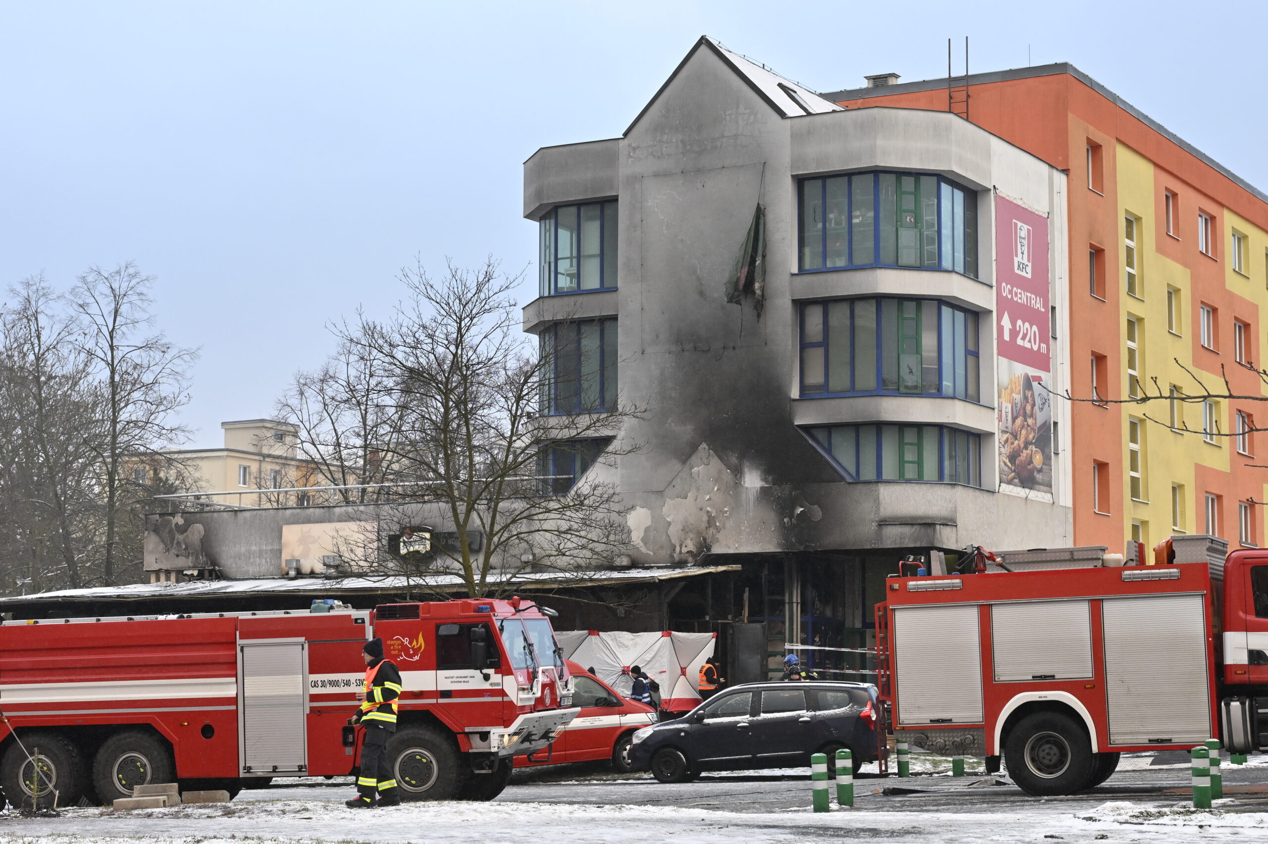 Feuerwehrfahrzeuge stehen vor einem Haus, dessen Fassade Brandspuren trägt.