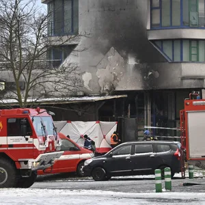 Feuerwehrfahrzeuge stehen vor einem Haus, dessen Fassade Brandspuren trägt.