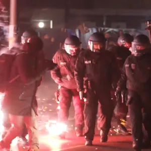Einsatzkräfte der Polizei in Berlin. Neben ihnen explodiert Feuerwerk