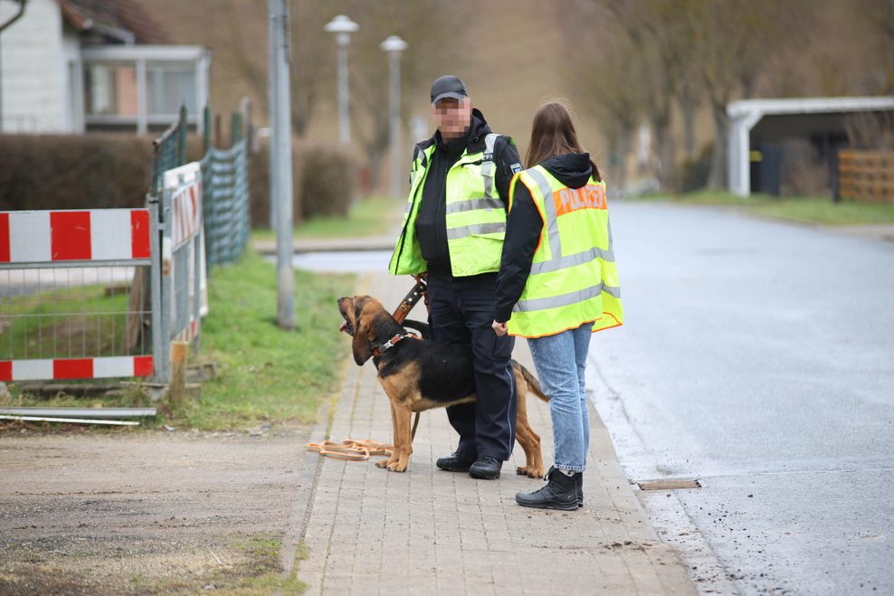 Polizisten mit Polizeihund suchen in der Nähe des Tatortes nach Spuren. Nach dem Fund einer Leiche in einem Haus in Rosdorf im Landkreis Göttingen gehen die Ermittler von einem Gewaltverbrechen aus.