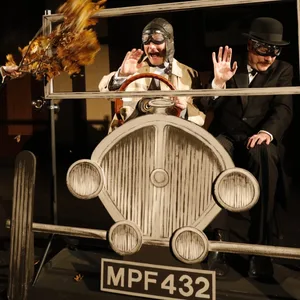 Zwei Schauspieler sitzen auf der Bühne in einem Cabrio-Gestell.