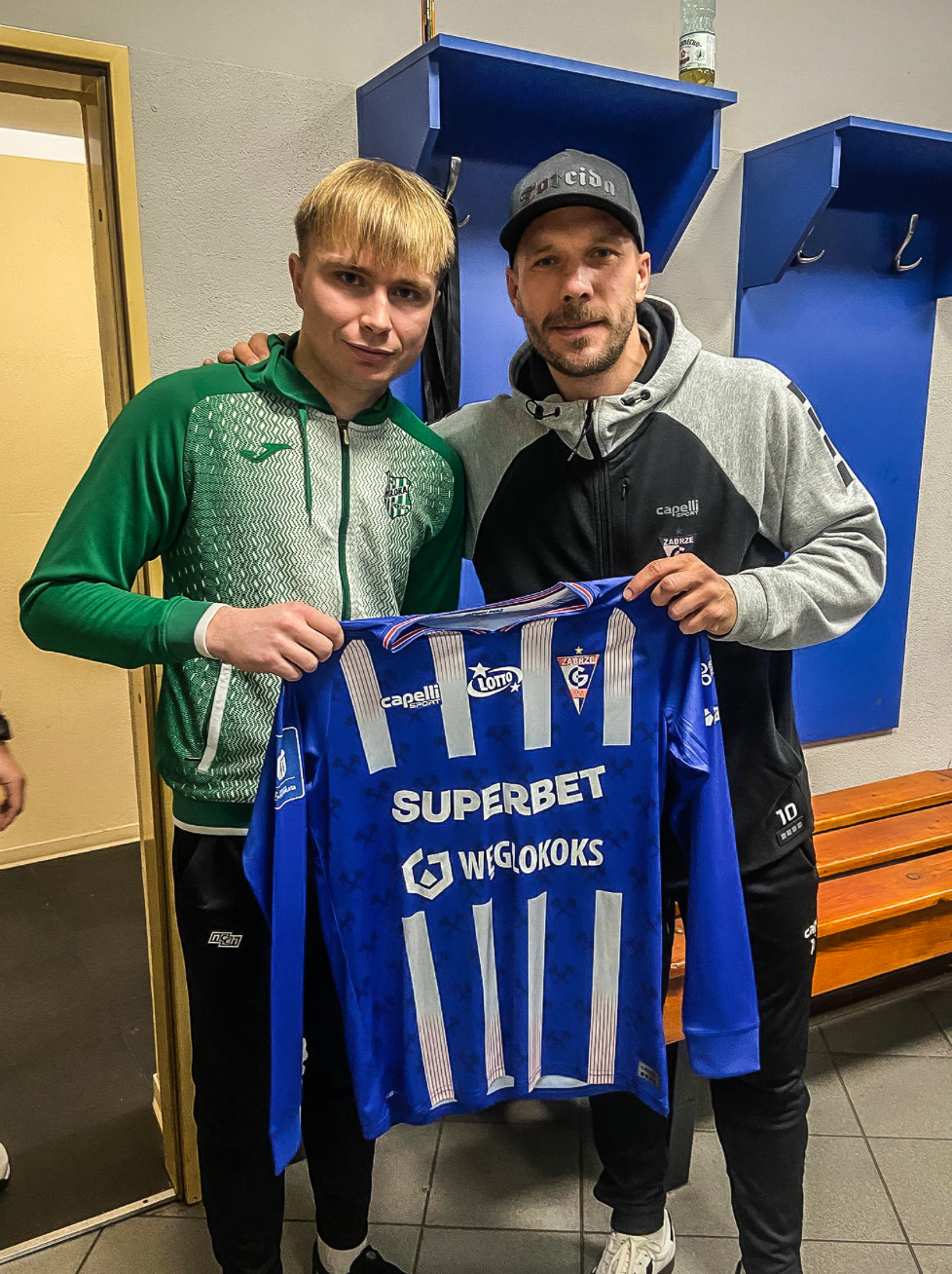 Lukas Podolski hält sein Trikot mit Jakub Siedlecki in die Kamera