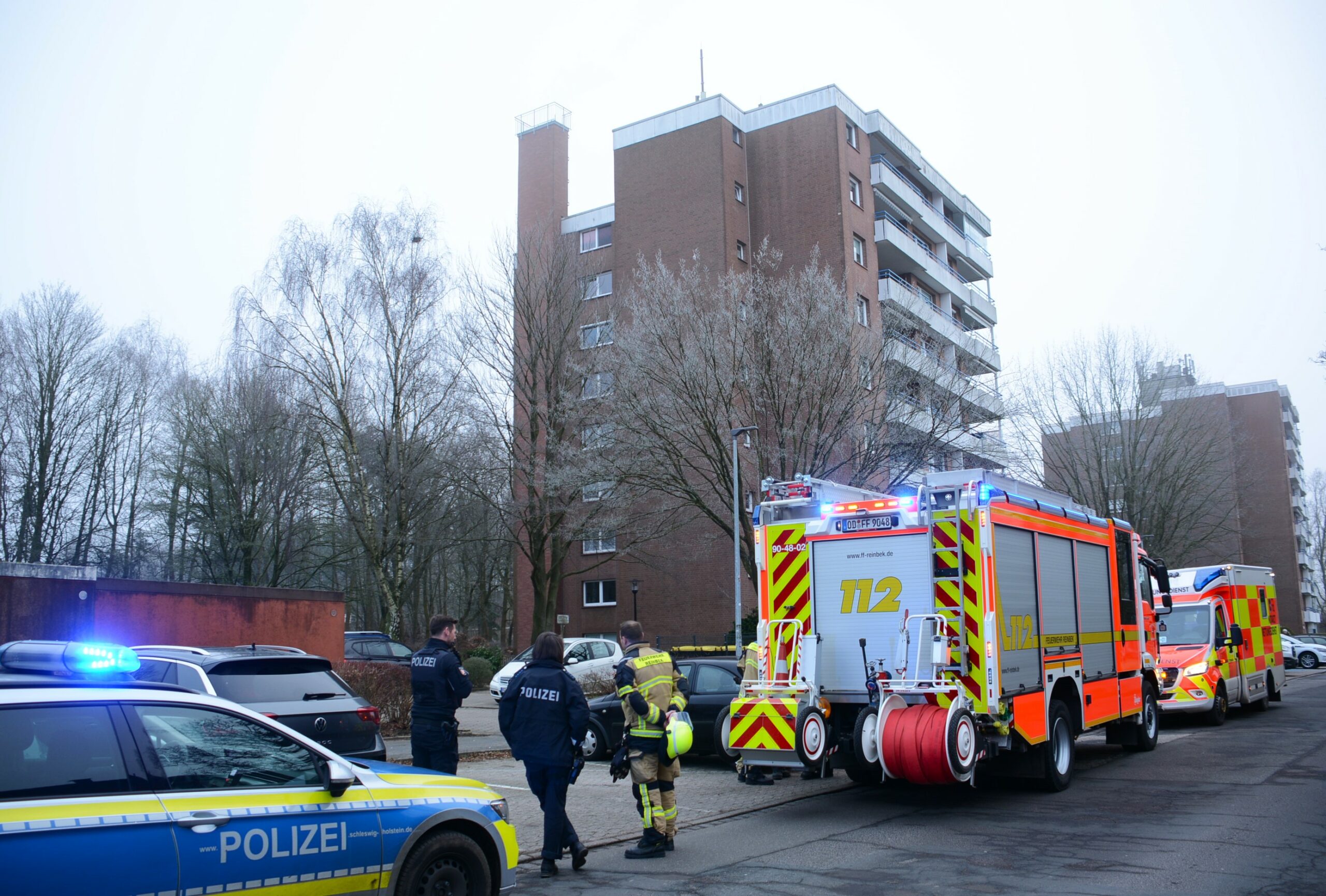 Polizei und Feuerwehr stehen vor einem Mehrfamilienhaus.