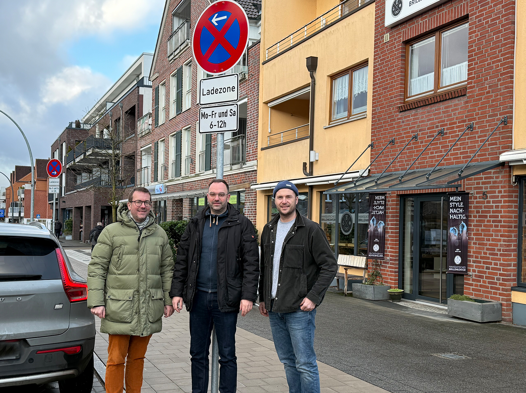 Drei Männer stehen unter einem „Ladezone“-Schild.