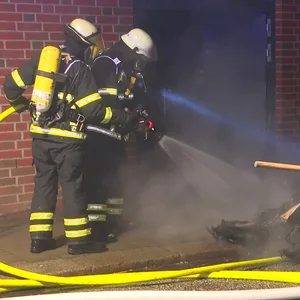 Feuerwehrleute löschen den verschmorten Müllcontainer.