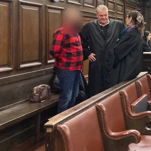 Der Angeklagte (l.) im Prozess um einen fast tödlichen Messerstich in einem Park steht vor der Urteilsverkündung im Gerichtssaal neben seinen Verteidigern.