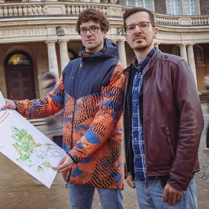 Die zwei Klimaforscher stehen vor dem Hauptgebäude der Universität Hamburg. Sie halten eine Karte die die Auswirkungen des Klimawandels auf soziale Gruppen zeigt.