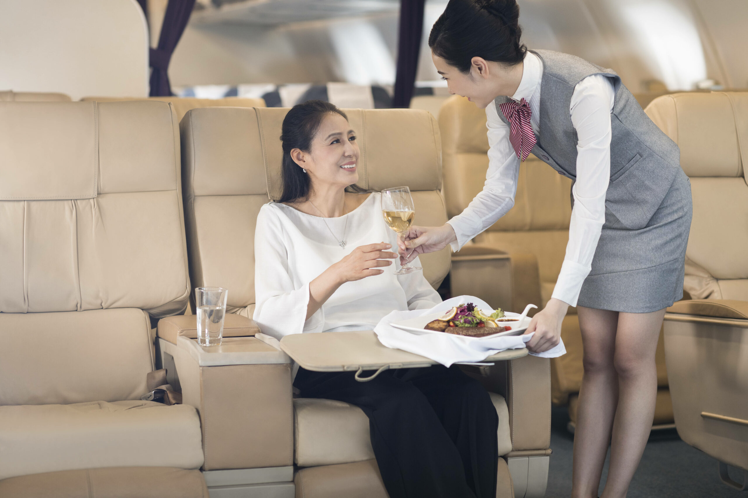 Eine Stewardess bringt einem Fluggast Essen und ein Getränk.