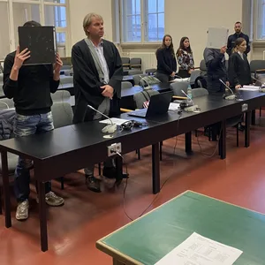 Die zwei Angeklagten stehen mit Mappen vor dem Gesicht in einem Saal im Landgericht Hamburg.