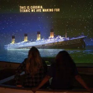 Zwei Menschen schauen auf eine Leinwand, man sieht dort die „Titanic“ untergehen