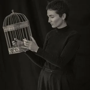Eine junge Frau hält einen Vogelkäfig in der Hand.