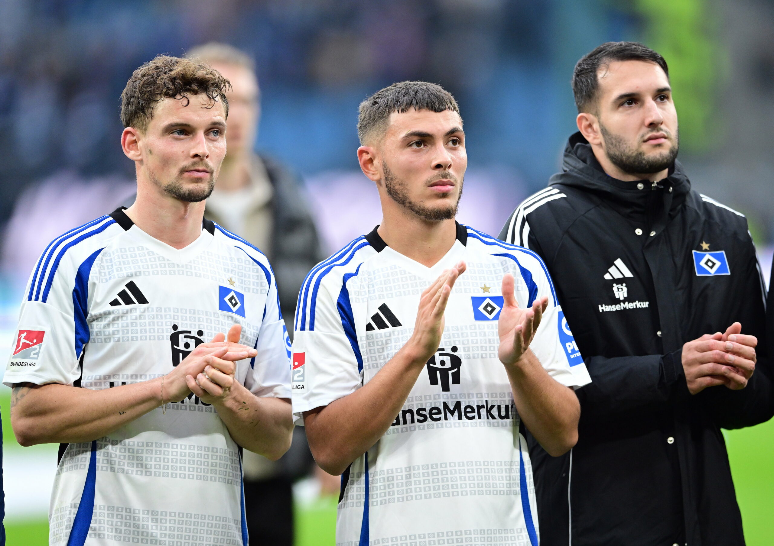 Moritz Heyer, William Mikelbrencis und Levin Öztunali stehen vor der HSV-Kurve.