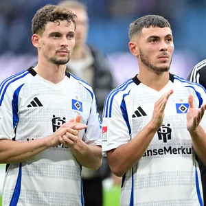 Moritz Heyer, William Mikelbrencis und Levin Öztunali stehen vor der HSV-Kurve.