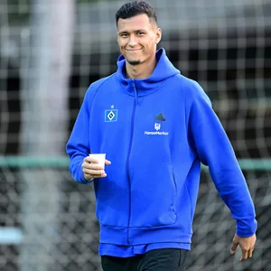 Davie Selke lächelt und hält einen Kaffeebecher in der Hand
