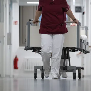 Eine Krankenpflegerin und ein Krankenpfleger schieben ein Krankenbett durch den Gang einer Station eines Krankenhauses.