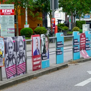 Ein Geländer an einer Straße fast vollständig mit Plakaten behängt