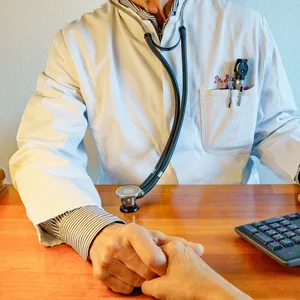 Arzt im Laborkittel mit Stethoskop am Schreibtisch hält die Hand eines Patienten.