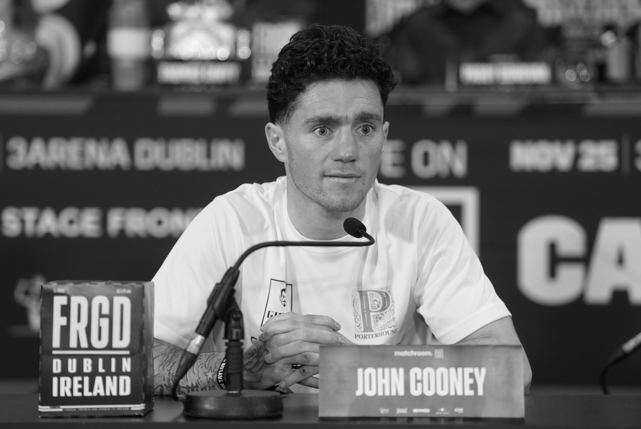 John Cooney sitzt bei einer Pressekonferenz.