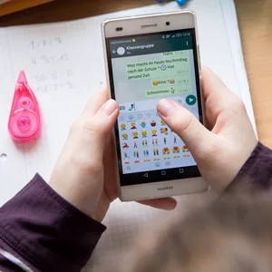 Eine Schülerin sitzt mit ihrem Handy und ihren Schulsachen an einem Schreibtisch.