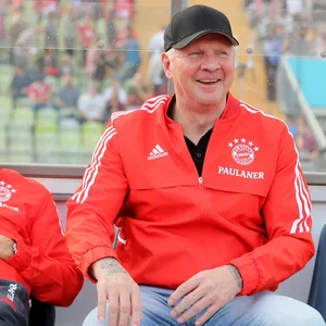 Stefan Effenberg sitzt in Bayern-Outfit auf der Bank und lacht
