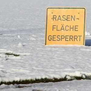 Ein Schild mit der Aufschrift „Rasenfläche gesperrt“ auf einem verschneiten Fußballplatz