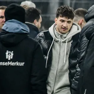 Noah Katterbach in Zivilkleidung vor der HSV-Bank neben Merlin Polzin