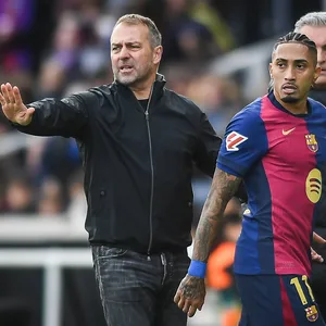 Hansi Flick hebt den Arm mit einer Stopp-Geste. Neben ihm ist Barcelonas Raphinha.