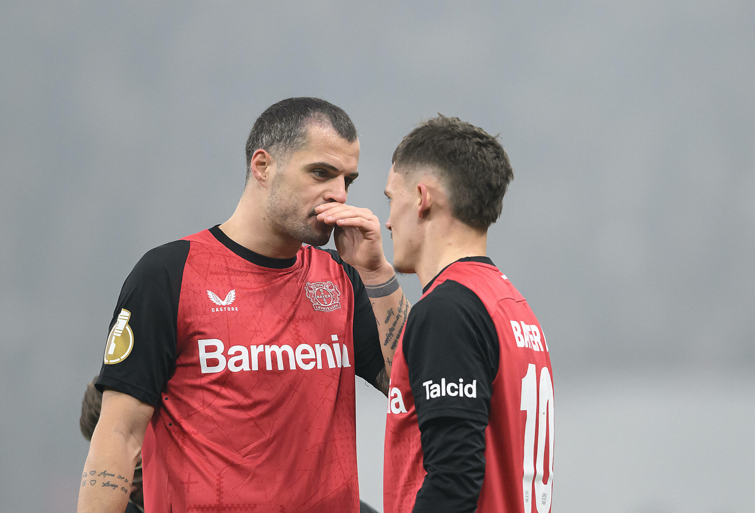 Leverkusens Granit Xhaka tauscht sich mit Florian Wirtz aus, hält sich dabei die Hand vor den Mund.