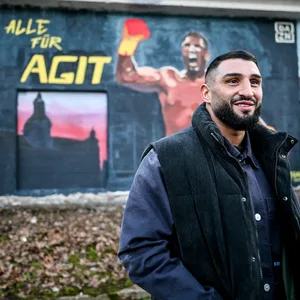 Agit Kabayel steht vor einem Graffiti was ihn selber zeigt