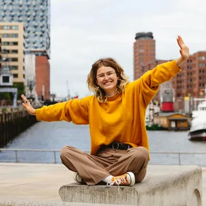 Happy young woman with arms outstretched sitting on bench at Elbphilharmonie model released, Symbolfoto, IHF01157