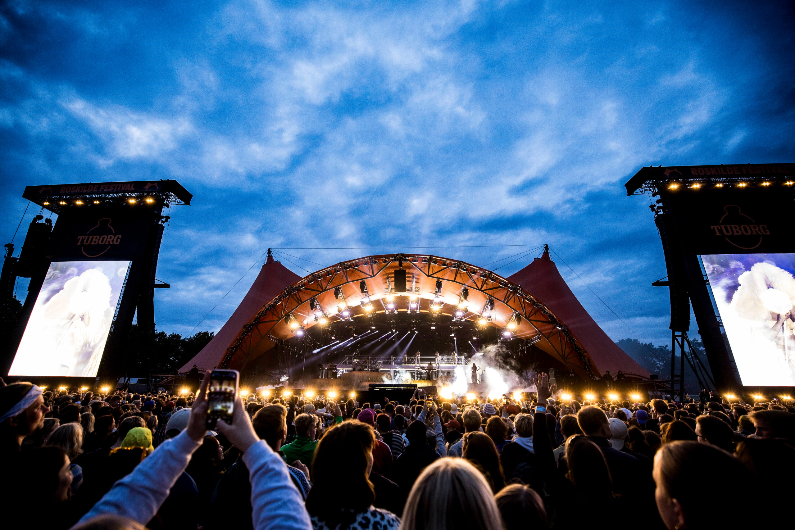 Besucher des „Roskilde“-Festivals feiern vor einer Bühne.