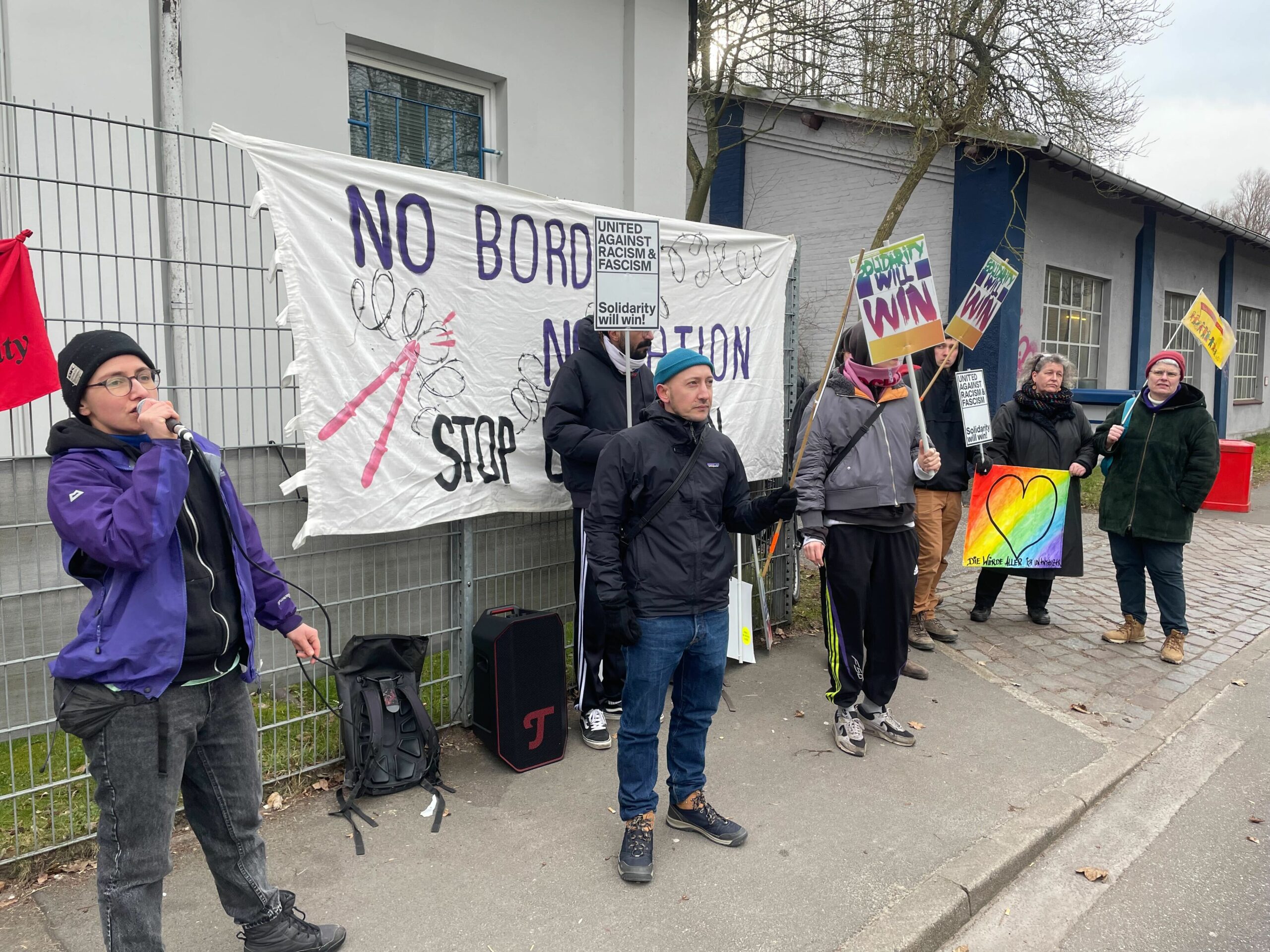 Ein Gruppe Demonstranten hat sich gegenüber des Eingangs aufgestellt.