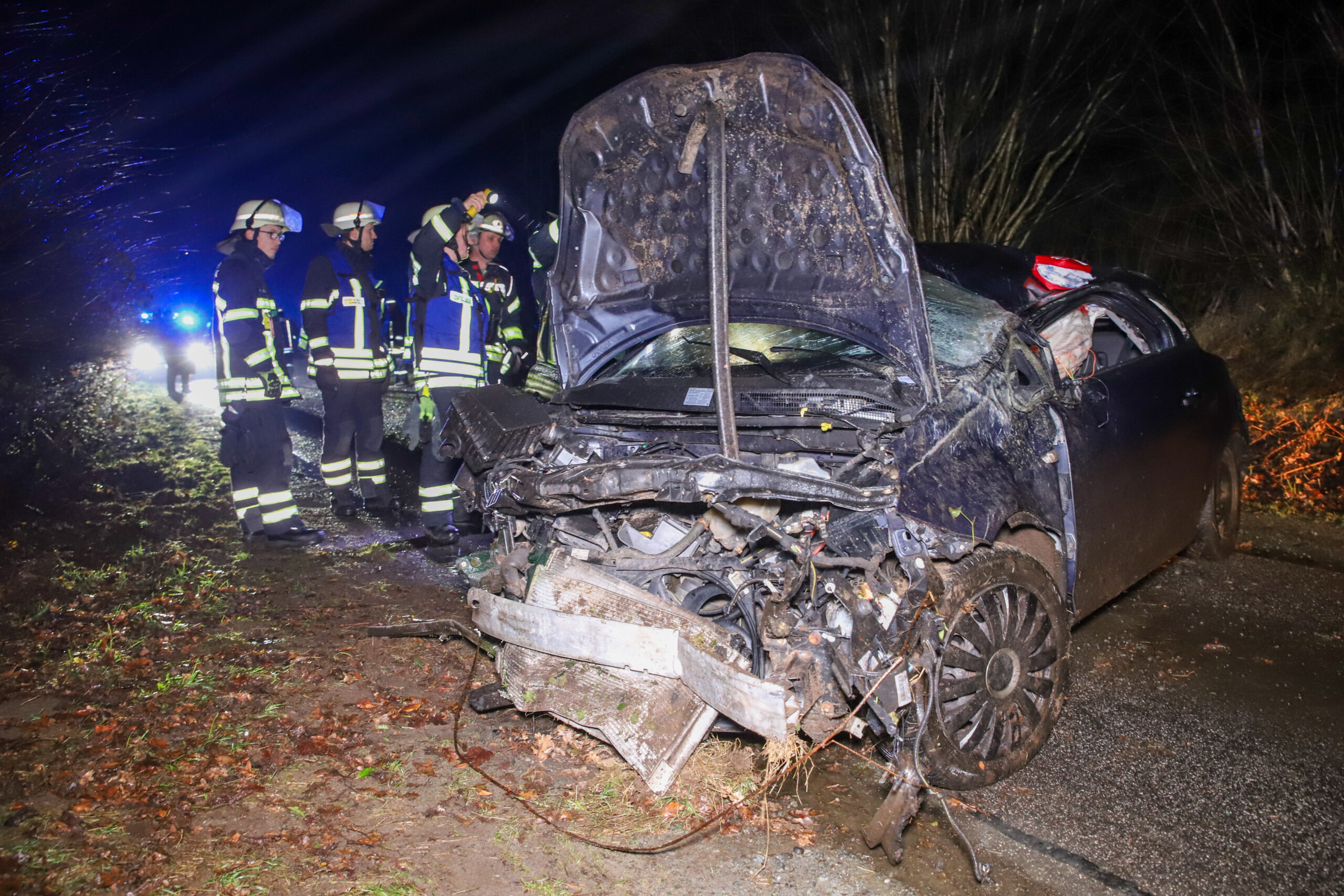 Feuerwehrleute stehen am Fahrzeugwrack.