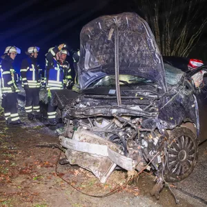 Feuerwehrleute stehen am Fahrzeugwrack.