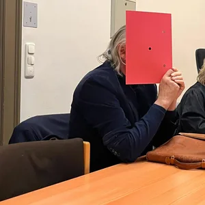 Charly A. vor Gericht: Der Mann mit den zurückgekämmten Haaren versteckt sein Gesicht hinter einem Aktenordner.