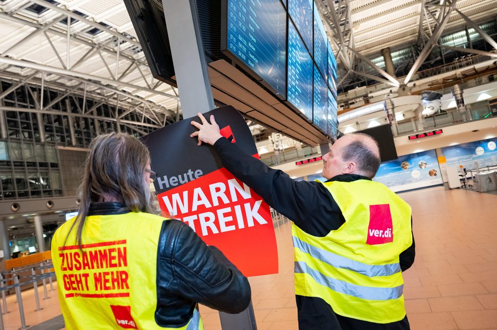 Verdi-Mitglieder hängen im Terminal 2 des Hamburger Flughafens ein Warnstreik-Plakat auf.