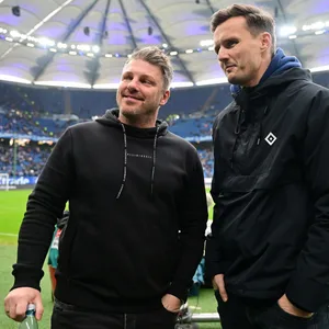 Lukas Kwasniok und Claus Costa lachen am Spielfeldrand im Volksparkstadion in eine Kamera