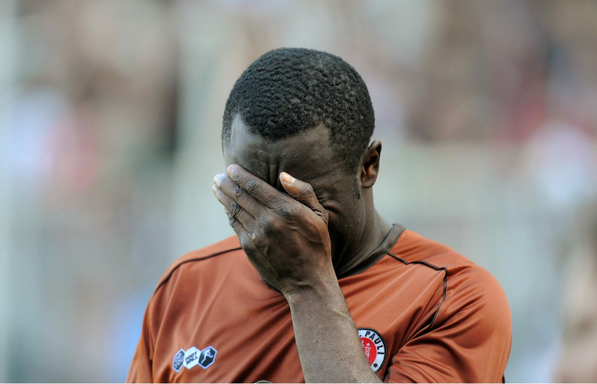 Gerald Asamoah vergräbt sein Gesicht in seiner linken Hand das St. Pauli-Trikot tragend.