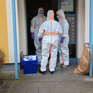 Polizisten in weißen Schutzanzügen in einem Hauseingang