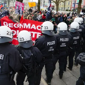 Eine Reihe an uniformierten Polizisten steht vor einer Gruppe Demonstranten