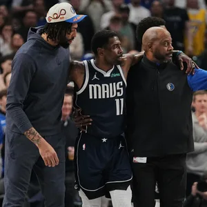 Kyrie Irving wird auf dem Spielfeld gestützt von zwei Betreuern der Dallas Mavericks