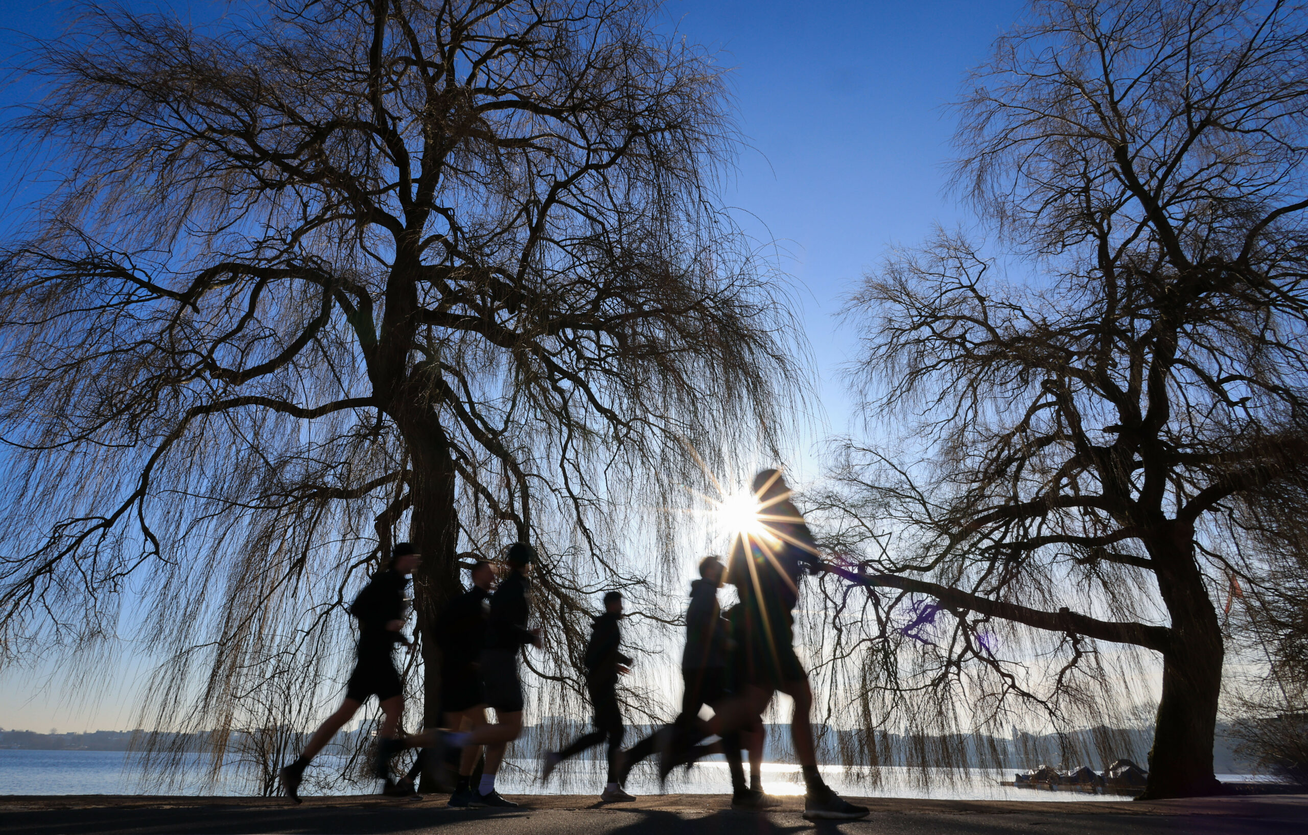 Ein Laufgruppe joggt bei strahlendem Sonnenschein an der Außenalster.