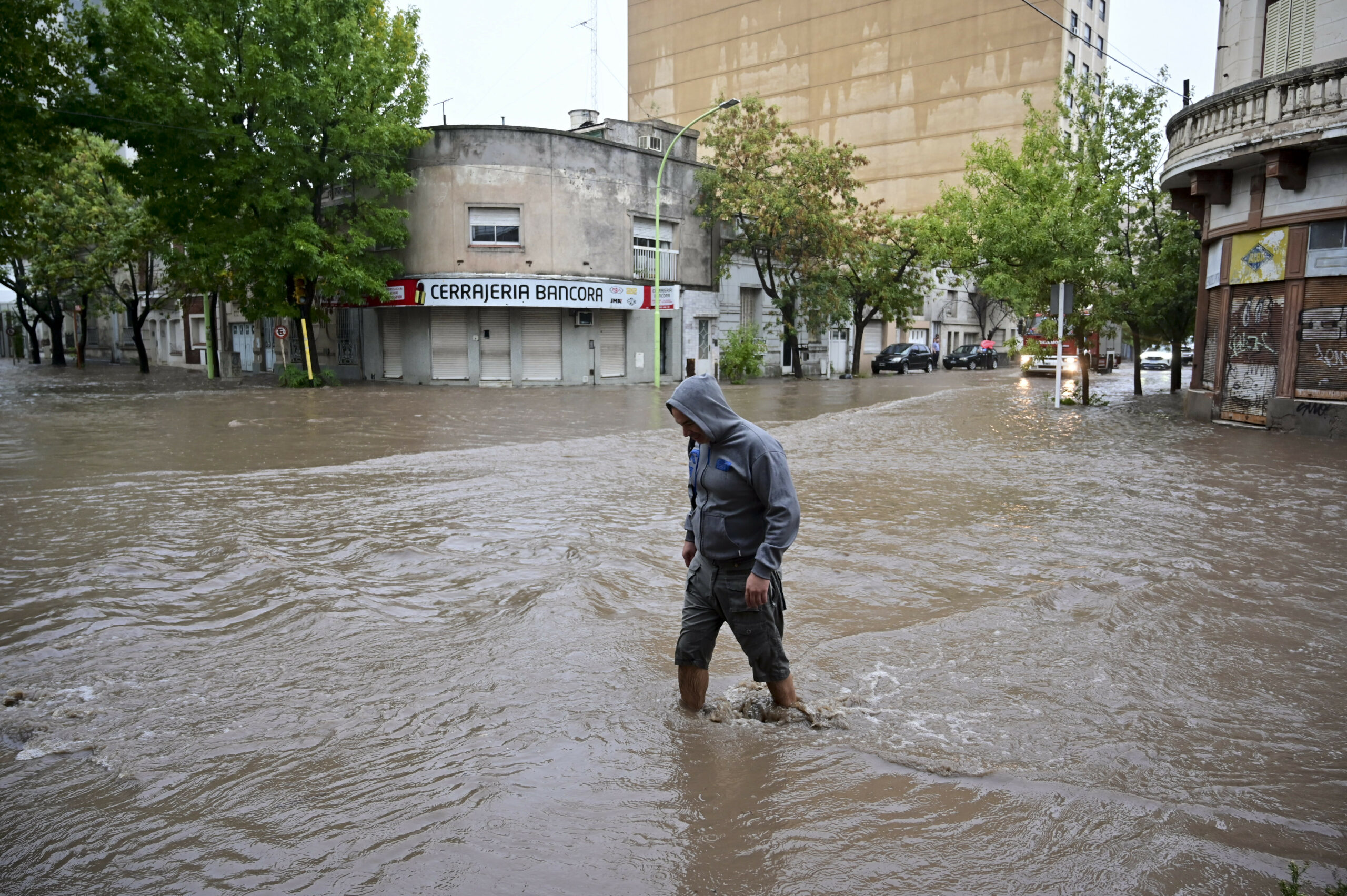 Ein Mann watet durch das Knie-hohe Wasser. Die komplette Straße ist überschwemmt.