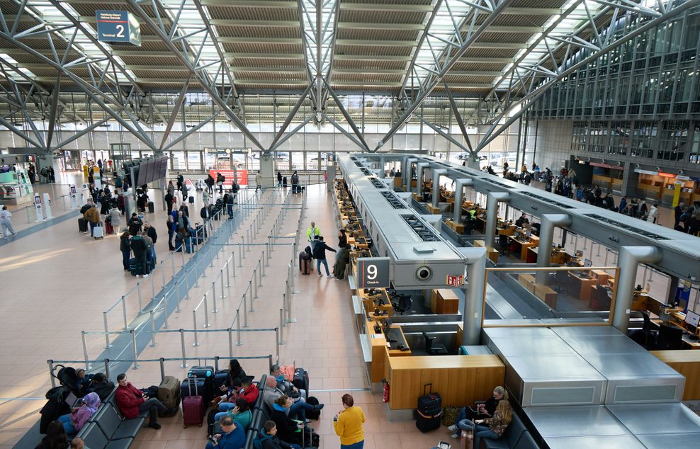 Passagiere stehen vor Schaltern am Flughafen in Hamburg. 