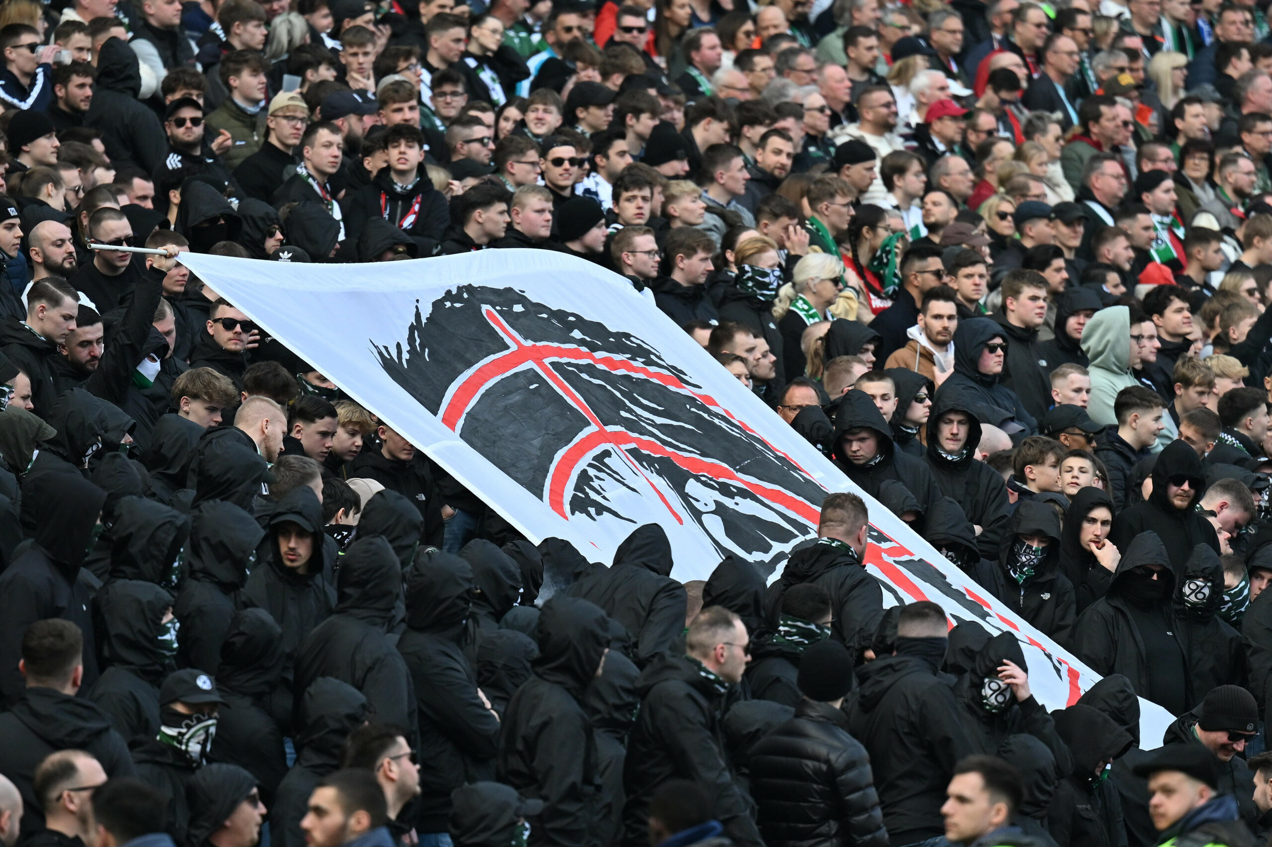 96-Fans halten ein Banner mit Fadenkreuz und einem Abbild von Niedersachsens Inniministerin Behrens